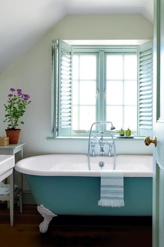 a countryside bathroom with aqua window frames, a turquoise bathtub and neutral textiles and potted blooms and plants