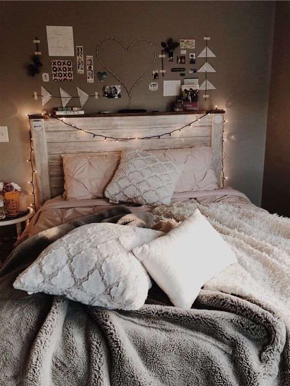 a cozy bedroom with taupe walls, a bed with a whitewashed headboard, cozy bedding, lights, a gallery wall and a table with candles