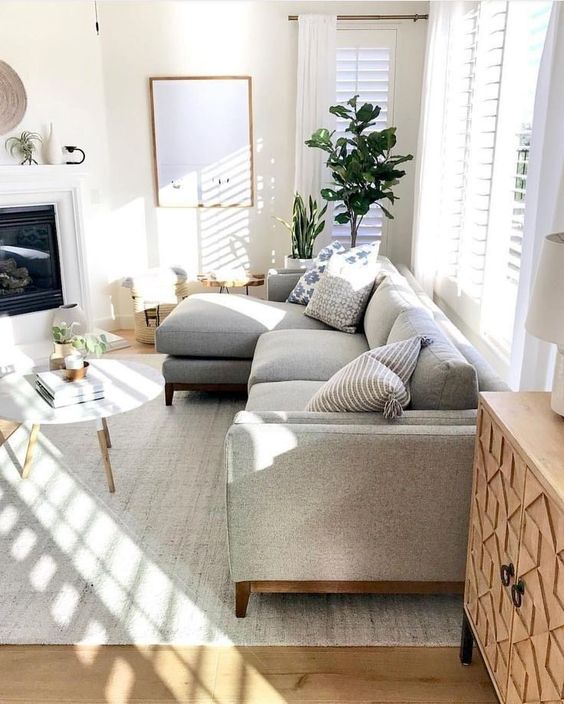 a cozy modern living room with a grey sofa, a built-in fireplace, a round table, potted plants and lots of natural light