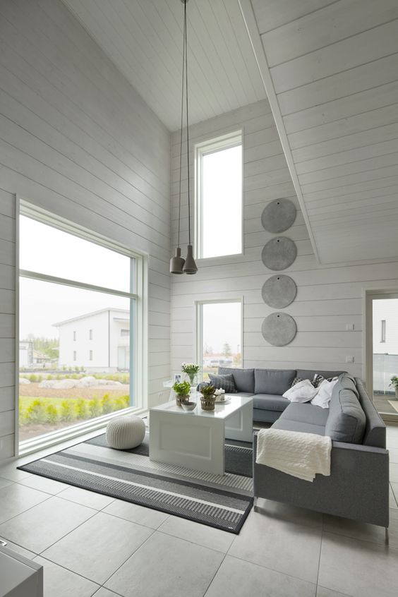 a double height living room with whitewashed wooden walls and a ceiling, a grey sofa, pendant lamps and a printed rug