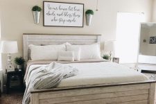 a farmhouse bedroom with tan walls, a whitewashed planked bed with neutral bedding, black nightstands, table lamps and buckets with greenery