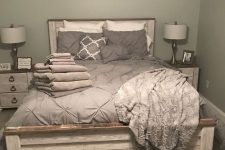 a grey farmhouse bedroom with a whitewashed planked wall, grey bedding, whitewashed nightstands, chic table lamps and artwork