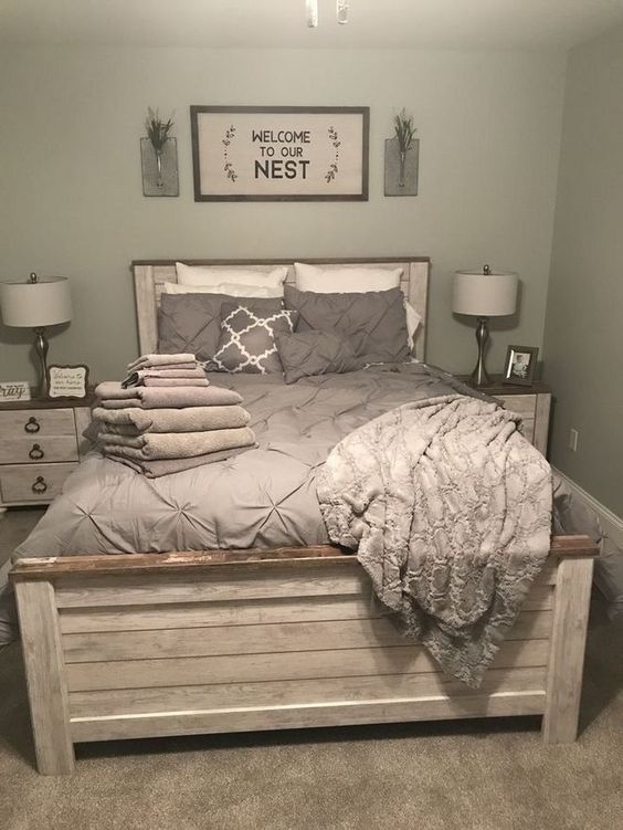 a grey farmhouse bedroom with a whitewashed planked wall, grey bedding, whitewashed nightstands, chic table lamps and artwork