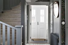 a grey farmhouse entryway with grey walls, a whitewashed floor, a wooden staircase and doors painted white