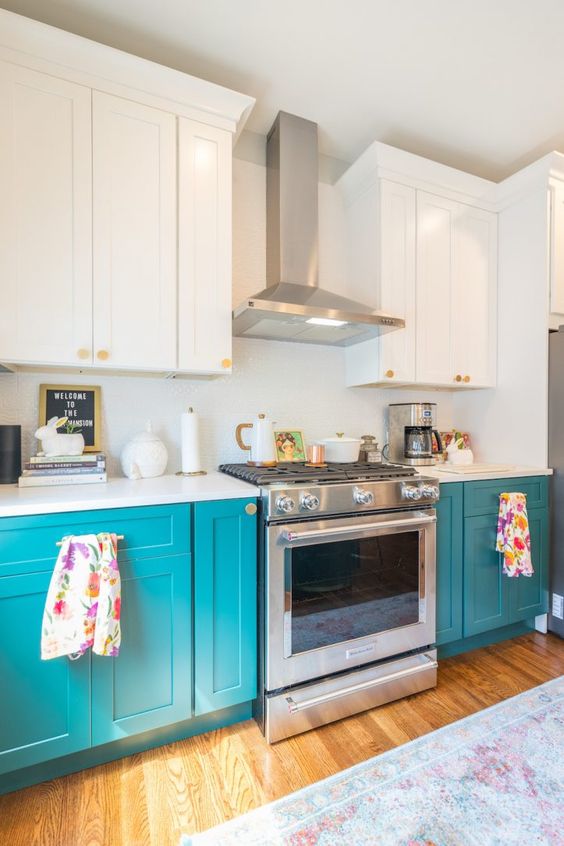 a lovely two-tone kitchen with white and turquoise shaker style cabinets, a white backsplash and stainless steel appliances