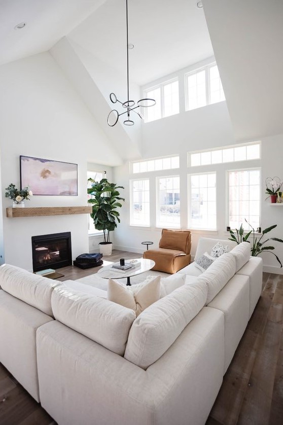 a modern neutral living room with a large white sofa, a fireplace with a mantel, a leather chair and a table, a pendant lamp