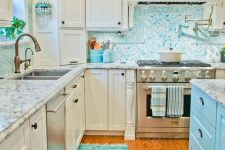 a modern white kitchen with shaker style cabinets, neutral stone countertops and a bright backsplash, a turquoise kitchen island, a rug and baskets