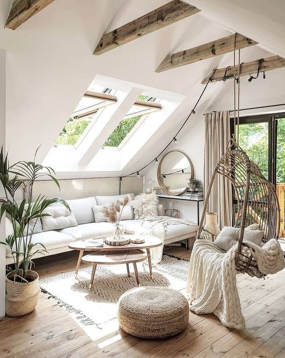 a neutral boho attic living room with skylights, beams, a suspended chair, wooden coffee tables