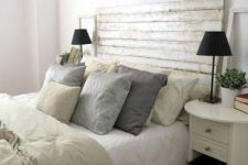 a neutral farmhouse bedroom with a bed with a whitewashed headboard, white nightstands, neutral bedding and black table lamps