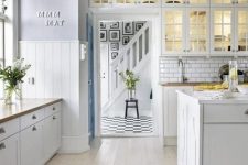 a neutral farmhouse kitchen with paneled walls, whitewashed floors, white cabinets and a white subway tile backsplash