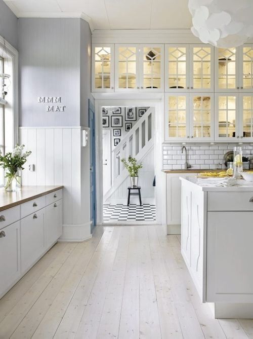 a neutral farmhouse kitchen with paneled walls, whitewashed floors, white cabinets and a white subway tile backsplash