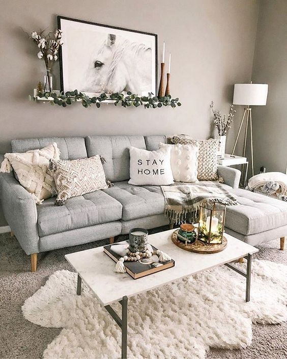 a pretty boho living room with a grey sofa, a white table, layered rugs, neutral tables, some candles and an artwork