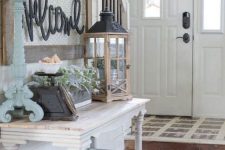 a pretty farmhouse entryway with a whitewashed vintage console table, a blue chest for storage, a candle lantern, a blue candleholder and some beautiful decor