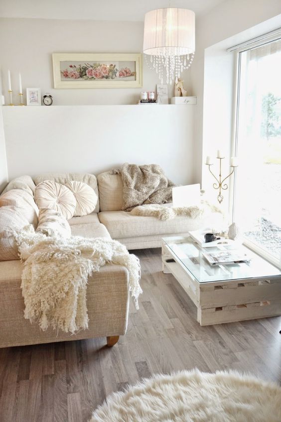 a small and neutral glam living room with a sectional sofa, a pallet table, a fur rug, a lamp with crystals