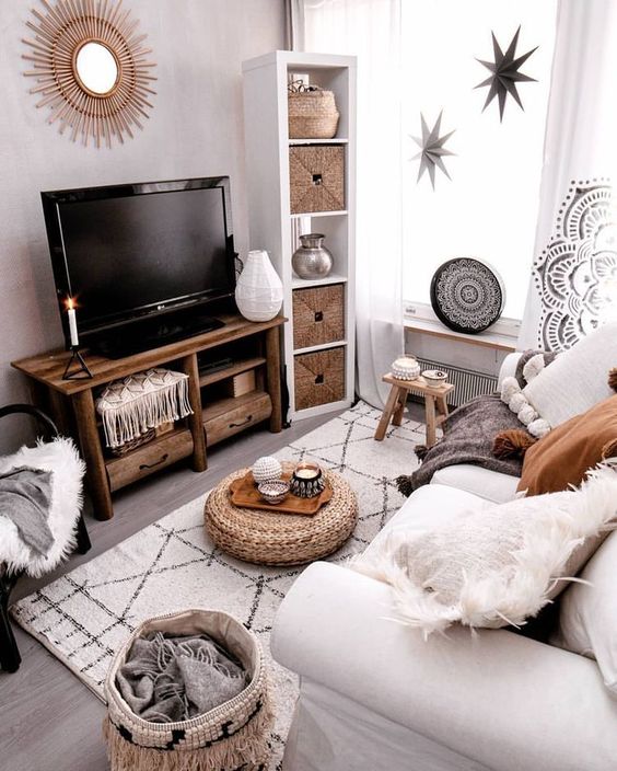 a small boho living room in neutrals, with a white sofa, woven items, a wooden TV unit, stars and a sunburst mirror on the wall