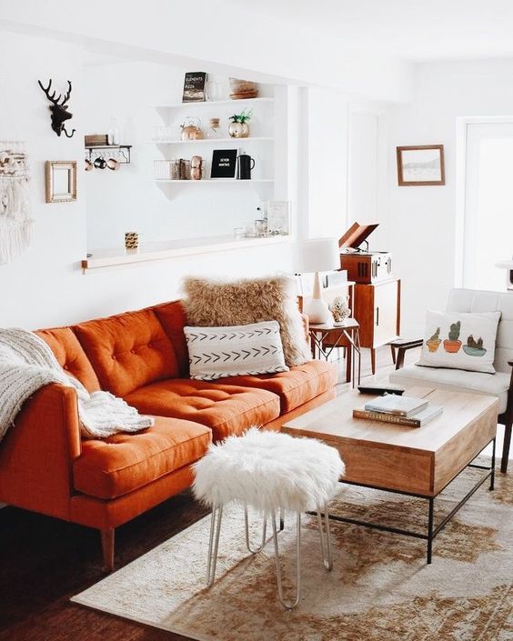 a small boho living room with a rust-colored sofa, printed pillows, a wooden table, mid-century modern furniture and a boho rug