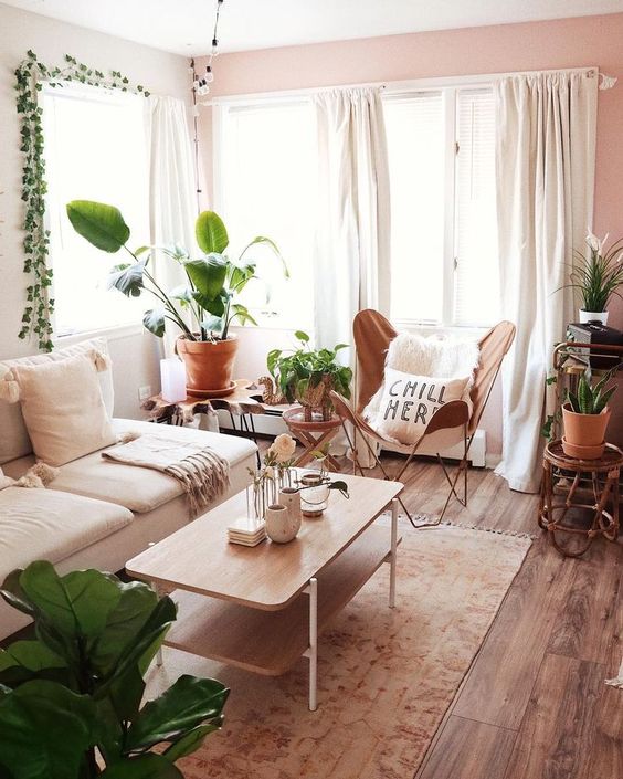 a small boho living room with a white sofa, a leather butterfly chair, a wooden table and lots of plants on stands