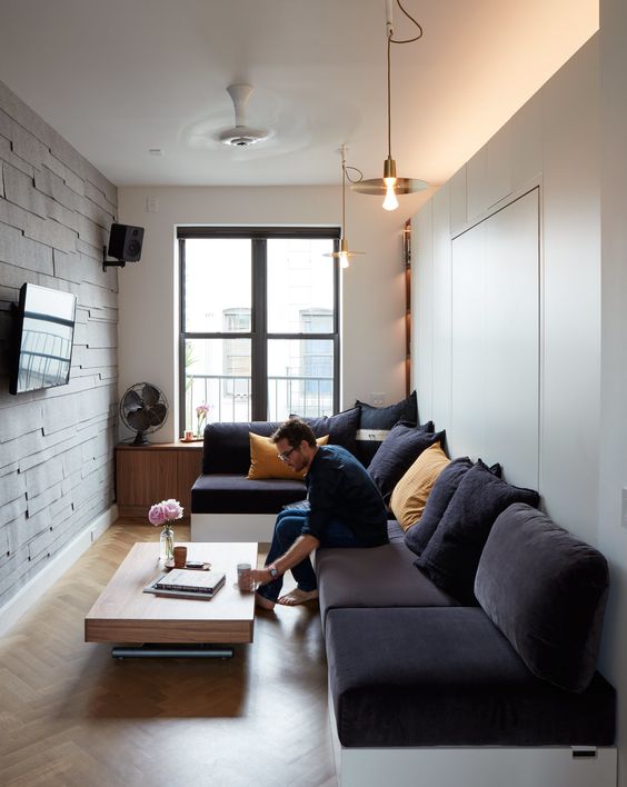 a small contemporary living room with a wood clad wall, a dark sectional, a wooden table and some simple lamps