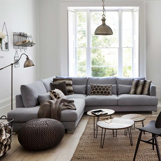 a small cozy living room with a grey sofa, knit ottomans, metal lamps, pin leg tables and a large window