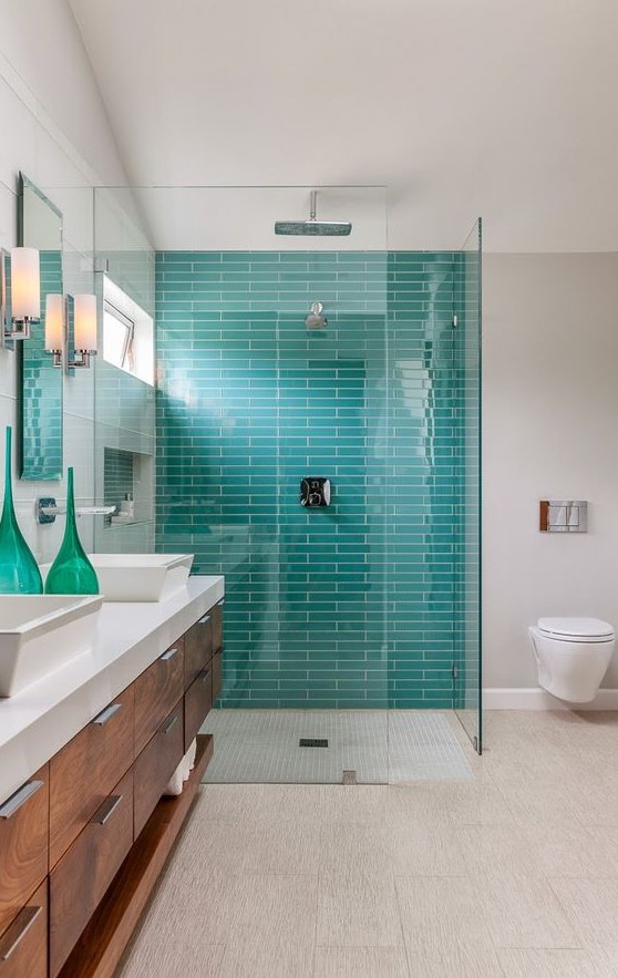 a stylish and bright bathroom with neutral tiles, tuquoise ones in the shower, a wooden vanity with a stone countertop and turquoise bottles
