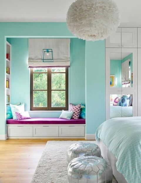 a turquoise bedroom with a window reading nook with built-in shelves, a bed with turquoise and white bedding and silver poufs
