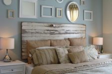 a vintage bedroom with a blue accent wall, a gallery wall of empty frames, a bed with a shabby whitewashed headboard, white nightstands and printed bedding
