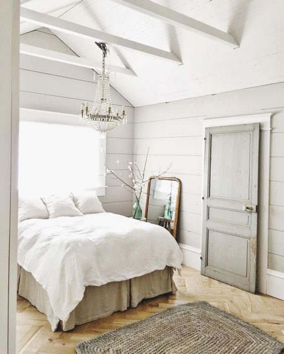 a vintage farmhouse bedroom with whitewashed wooden walls, vintage furniture, a crystal chandelier and a mirror in a wooden frame