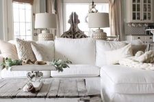 a vintage farmhouse living room with a white sectional, a whitewashed and distressed pallet coffee table, cool lamps and some greenery