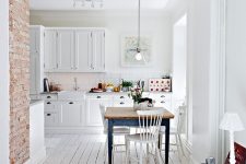 a vintage-inspired kitchen with white walls, a whitewashed floor, white cabinets and a blue dining table