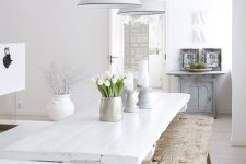 a vintage-inspired white kitchen with white walls and a whitewashed floor, white and stained furniture plus greenery