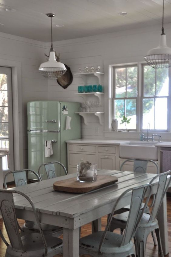a white Scandinavian kitchen with white cabinets, a green fridge, a whitewashed table and chairs, pendant lamps and open shelves