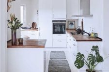a white kitchen with a whitewashed floor, white cabinets with butcherblock countertops and potted greenery