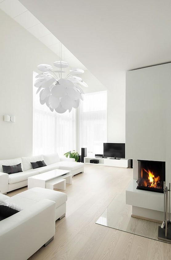 a white minimalist living room with simple and comfy furniture, a built-in fireplace, a petal lamp and much natural light