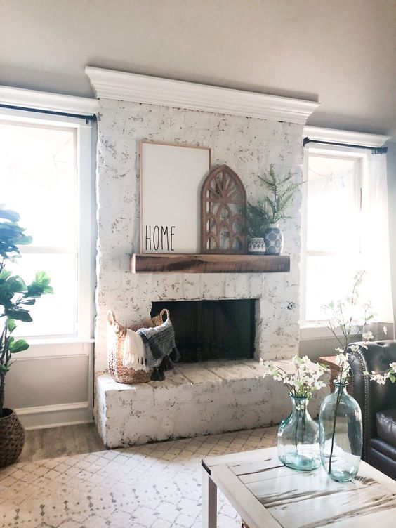 a whitewashed brick fireplace with a wooden mantel, rustic decor and potted greenery is rustic and cozy