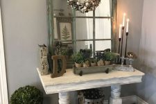 a whitewashed console table, potted plants, a cotton wreath, candles and candleholders for a refined vintage entryway