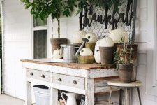 a whitewashed gardening table with lots of pumpkins, greenery, watering cans and jugs is a cool idea for a rustic porch