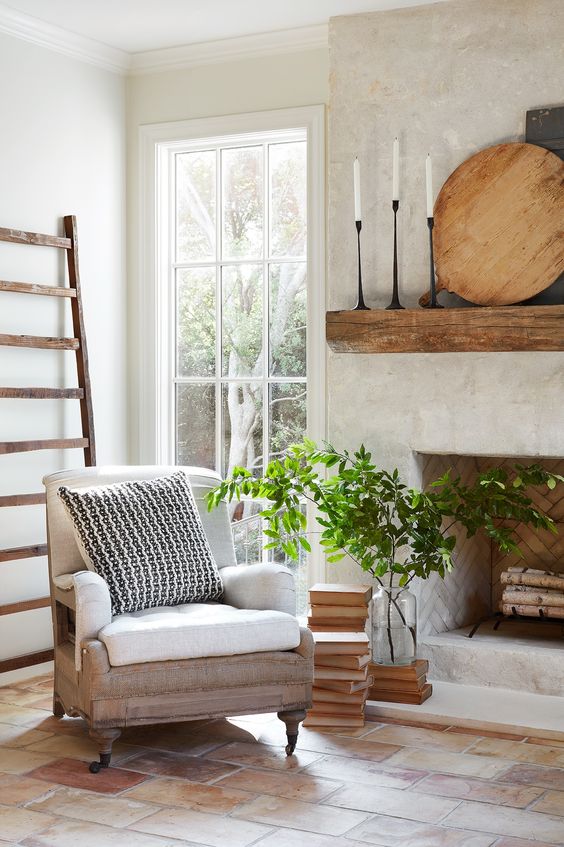 a whitewashed plaster and brick fireplace with firewood, a wooden mantel with candles and stacks of books
