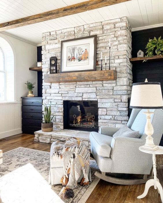 a whitewashed stone fireplace with a rough wooden mantel, vintage decor and a potted plant brings a farmhouse feel