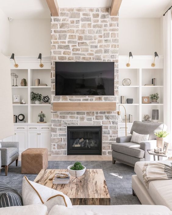 a whitewashed stone fireplace with a wooden mantel and storage units on each side of it is a cozy and chic touch to the room decor