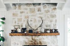 a whitewashed stone fireplace with a wooden mantel with candles, antlers and more rustic decor for a cozy feel
