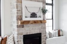 a whitewashed vintage brick fireplace with a mantel with some decor and windowsill seat next to it