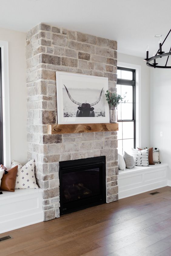 a whitewashed vintage brick fireplace with a mantel with some decor and windowsill seat next to it