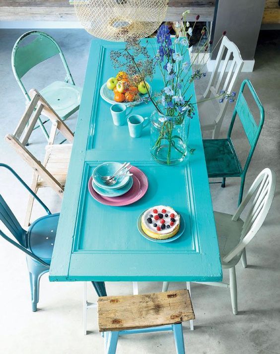 an eclectic dining nook with a turquoise door as a table, mismatching chairs and bright tableware is a cool space