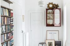 an eclectic entryway with white walls, a whitewashed floor, vintage furniture and a pendant lamp plus artworks
