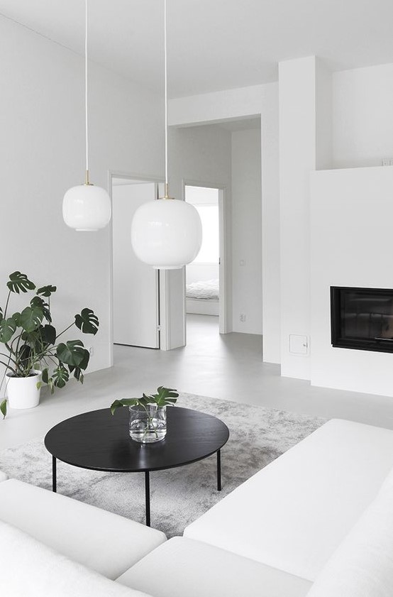 an ultra-minimalist living room with a white sectional, a built-in fireplace, a black table and white pendant lamps