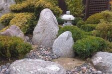 a Japanese garden with pebbles, large rocks, greenery, small trees and stone lanterns looks very soothing