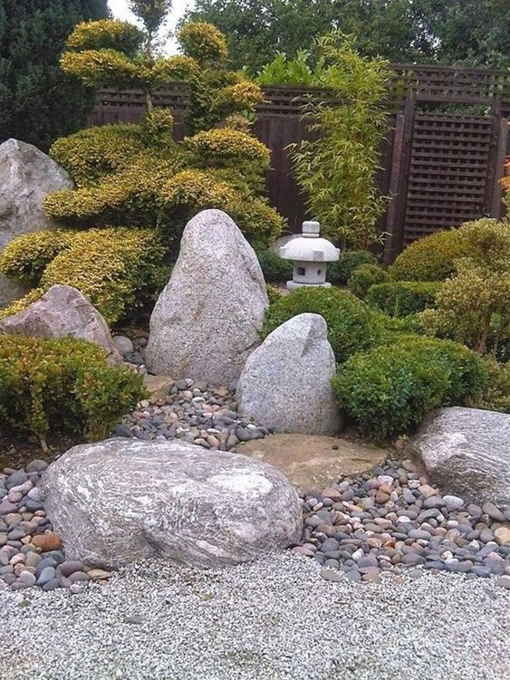 a Japanese garden with pebbles, large rocks, greenery, small trees and stone lanterns looks very soothing