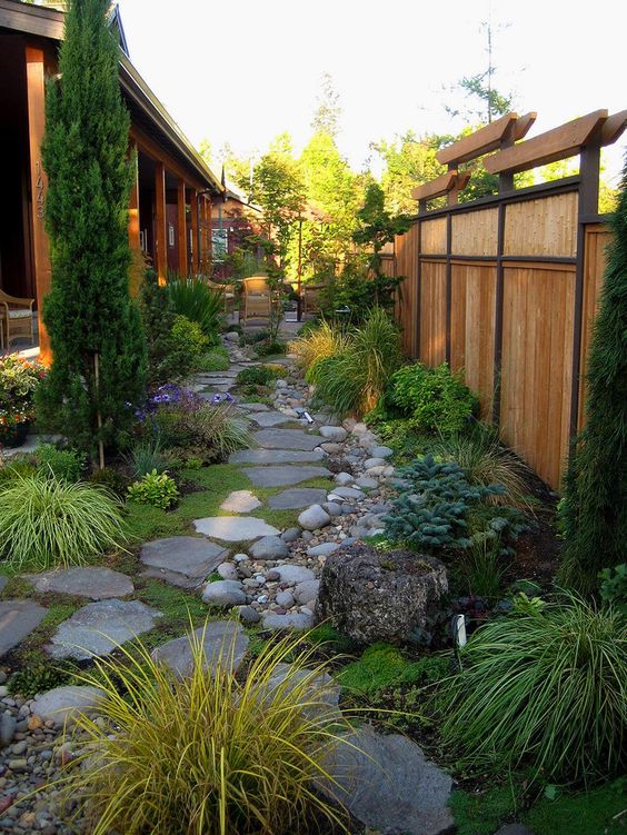 a Japanese-inspired garden with rock tiles, pebbles, tree stumps, greenery, grasses and a tall tree for a zen look