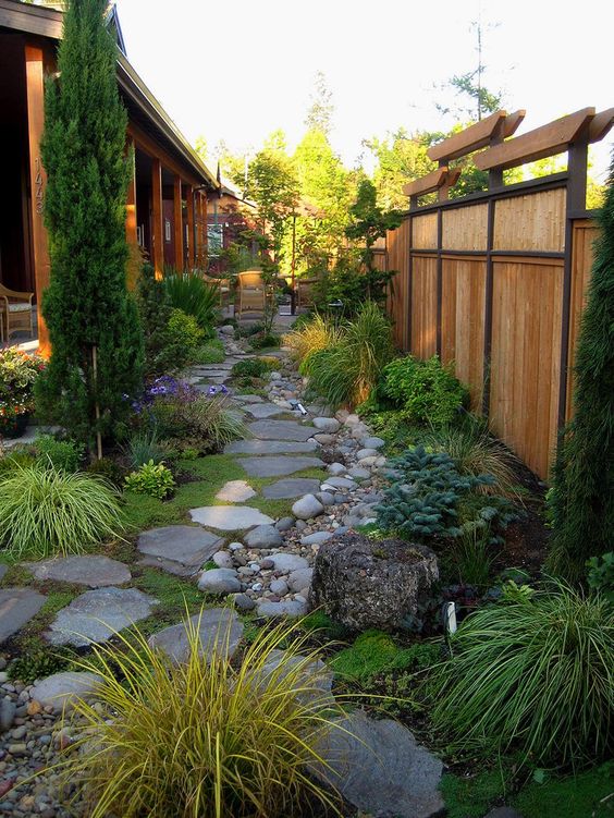 un jardín de inspiración japonesa con tejas de roca, guijarros, tocones de árboles, vegetación, pastos y un árbol alto para una apariencia zen