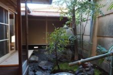 a beautiful Japanese backyard with pebbles and rocks, some moss, a couple of trees and a traditional bamboo fountain in the center